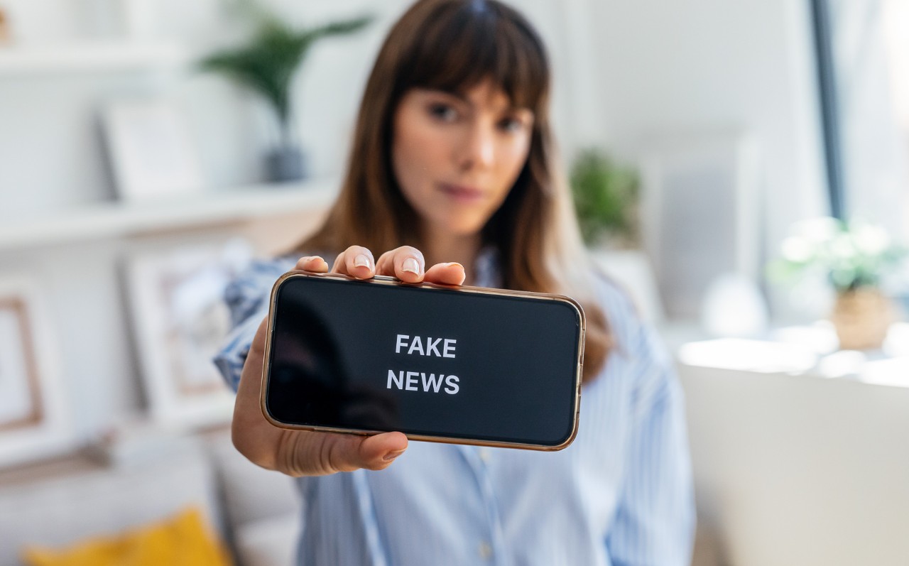 A woman holds up a phone screen that reads fake news.