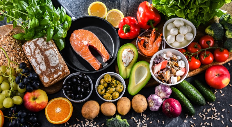 A spread of foods that make up the Mediterranean diet, including avocado salmon, olives, tomatoes and leafy greens