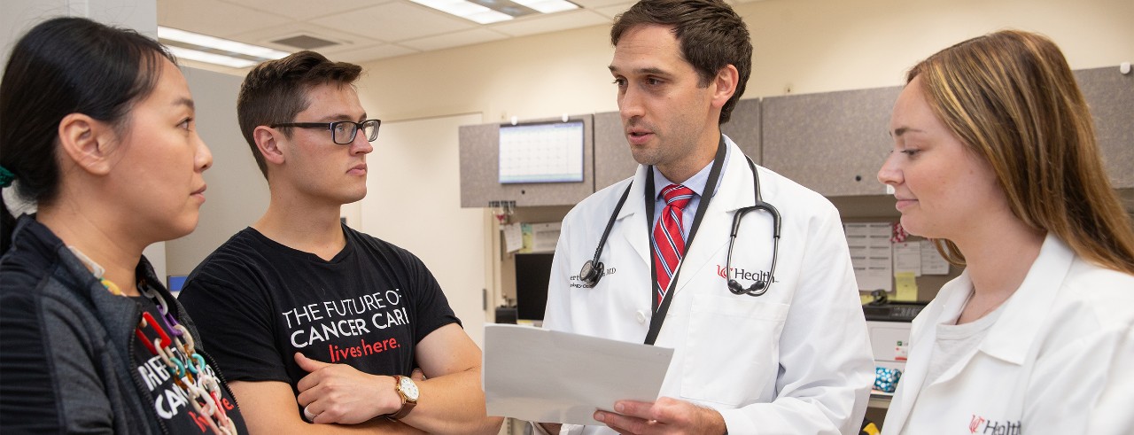 Two people wearing black T-shirts and two people wearing white lab coats have a conversation in the clinic