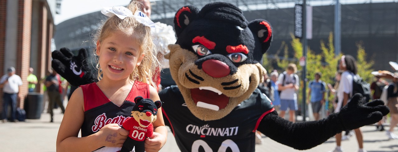 Little girl dresses in UC swag  gets a hug from the UC Bearcat Mascot