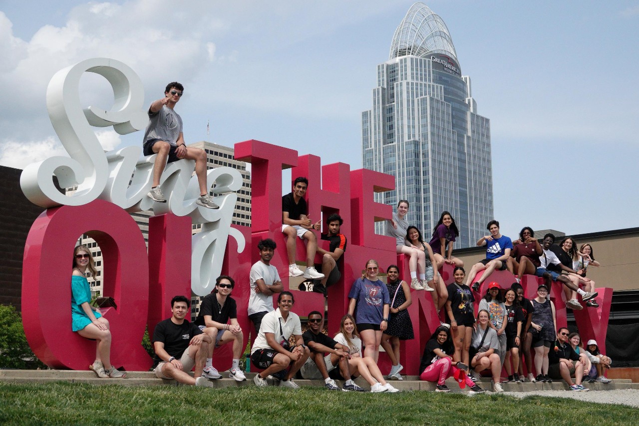 Students pose around giant 3D signage that says "Sing the Queen City"