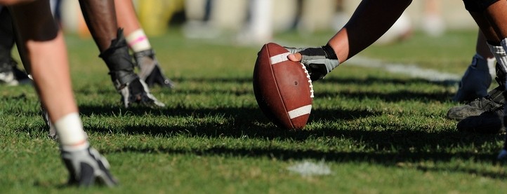 football on field and hands of players on the ball for the hike