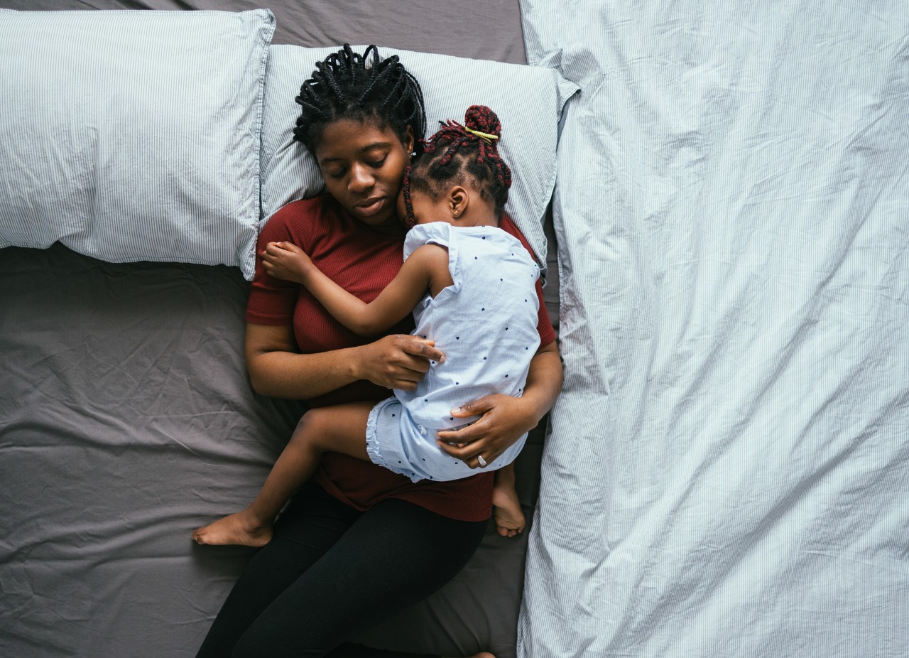 Parent laying on bed holding sleeping child