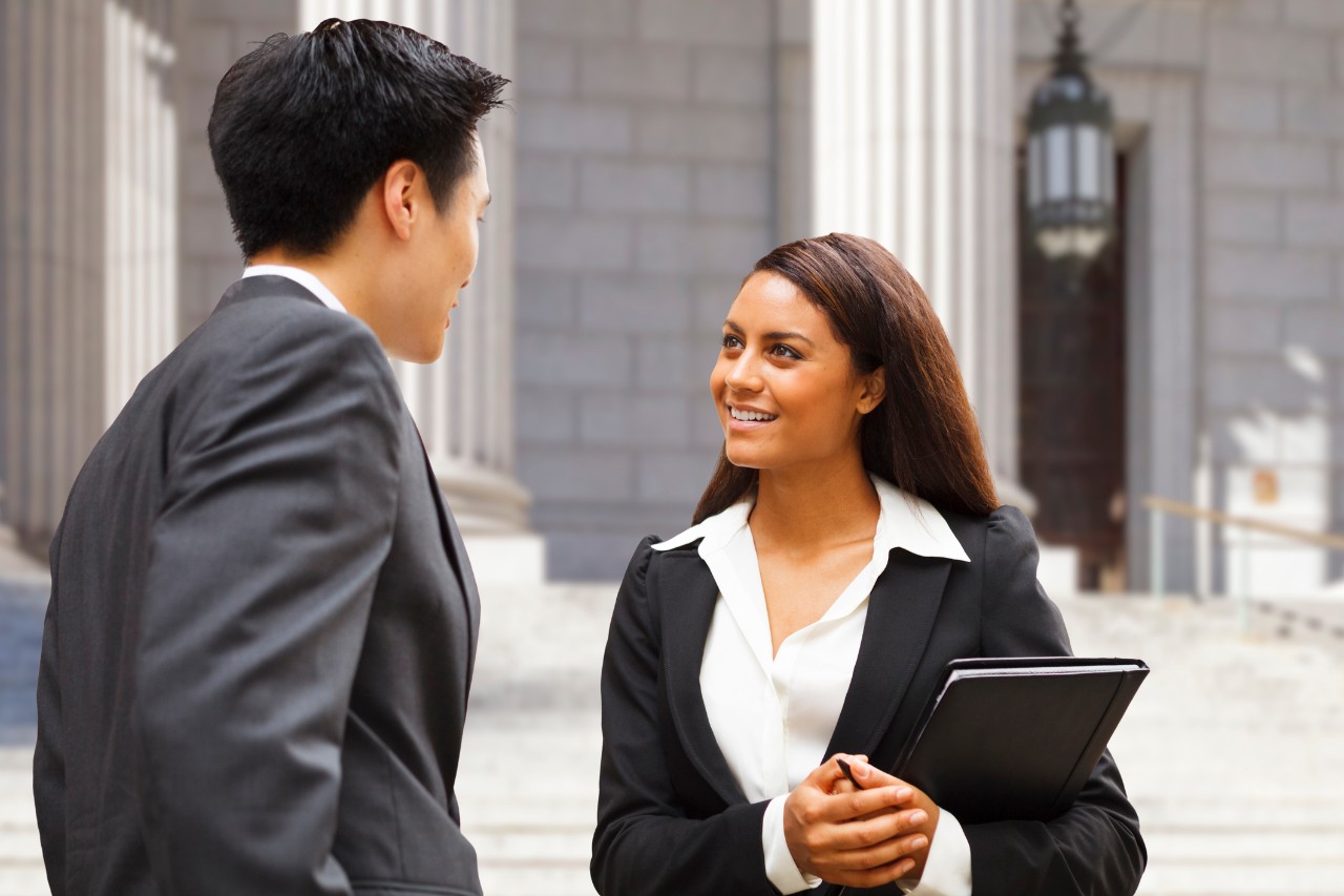 Two young lawyers hold conversation in front of courthouse