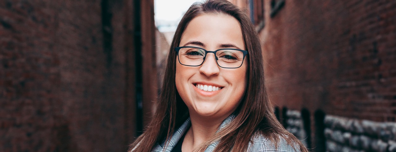 woman stands smiling in a brick-walled alley