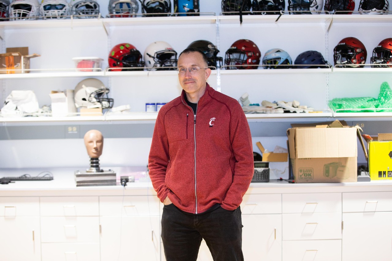 UC Professor Eric Nauman stands in front of shelves of sports helmets.