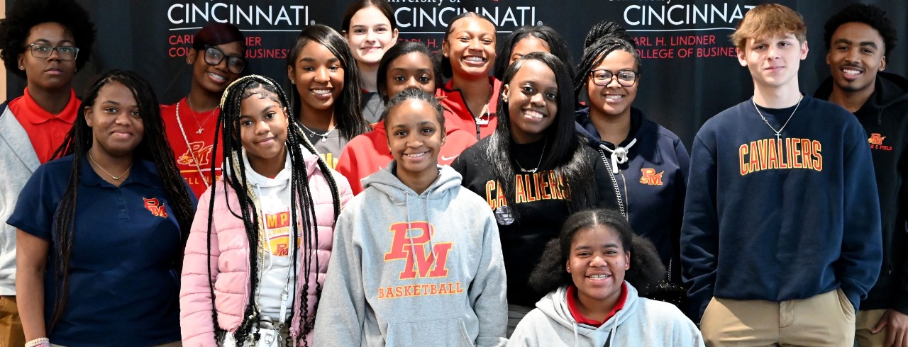 Thirteen students against a black backdrop pose in the Lindner Hall atrium