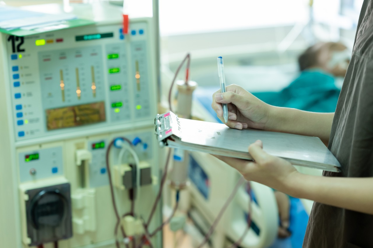 A health care worker with a clipboard checks outputs from a dialysis machine.