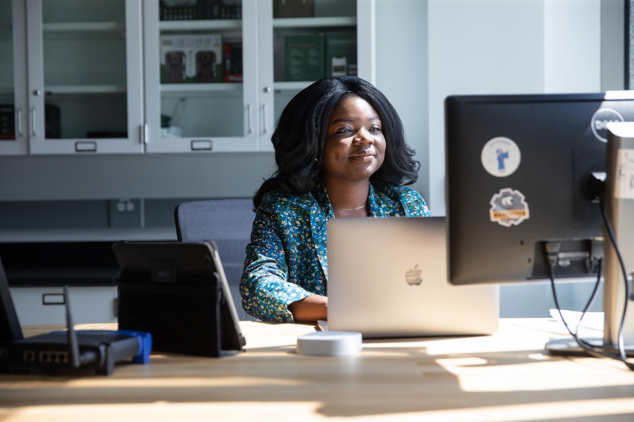 Grad student smiling at desk with multiple computer screens