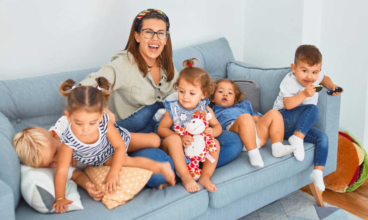 A woman sits on a couch with five children.