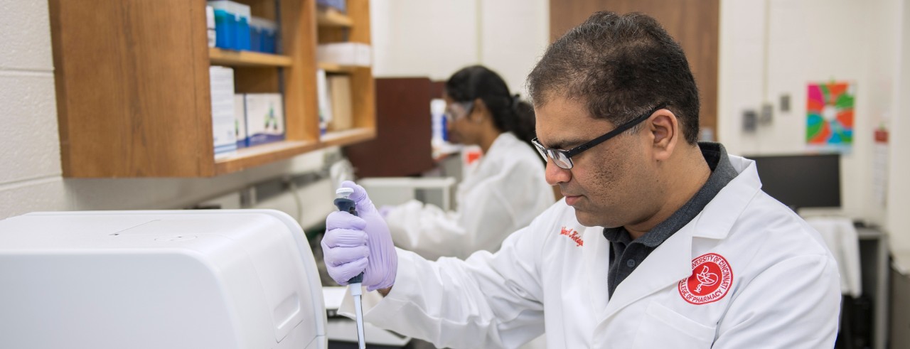 Nalinikanth Kotagiri wears a white coat and pipettes a sample at a bench in the laboratory