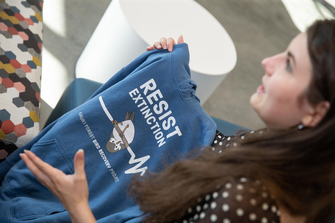 Ella Marcil holds up a hoodie promoting the plight of the endangered akikiki with the words resist extinction.