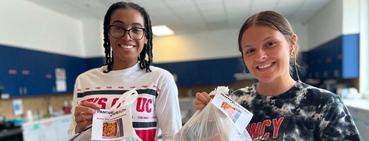 University of Cincinnati students Kindall Coley and Kassidy Meyer hold up bags with food.