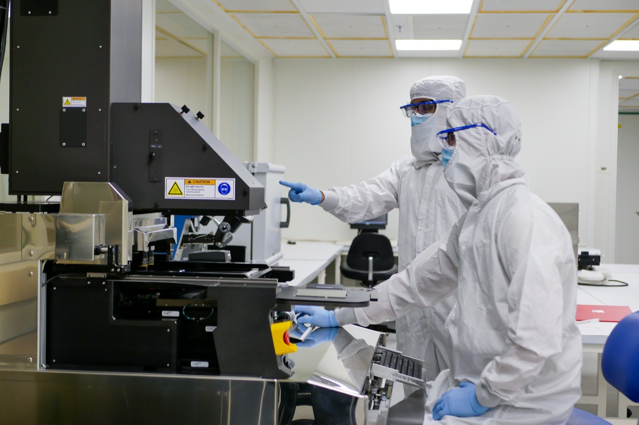 Two people in white protective suits work with equipment in a cleanroom