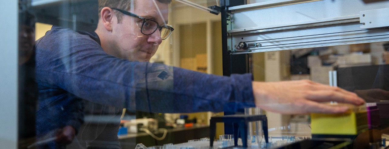 A chemistry student reaches for samples inside a robotic pipette machine.