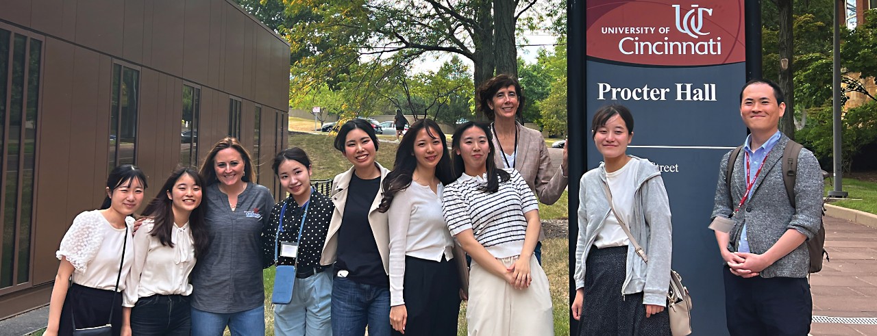 Chiba University Students and UC nursing faculty standing in front of Procter Hall sign