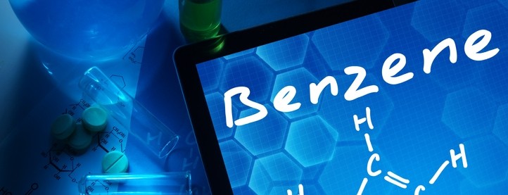 The word "Benzene" and its chemical diagram on a tablet screen with lab equipment and pills in the background