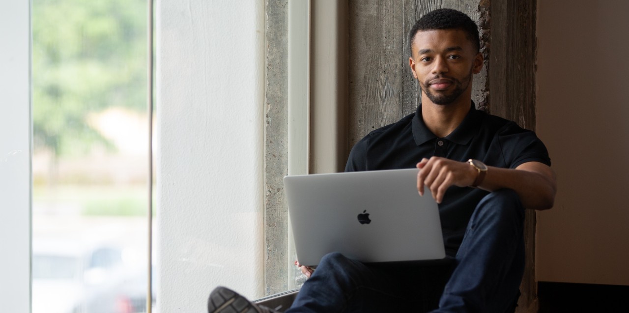 A man sitting with a laptop looks at the camera.