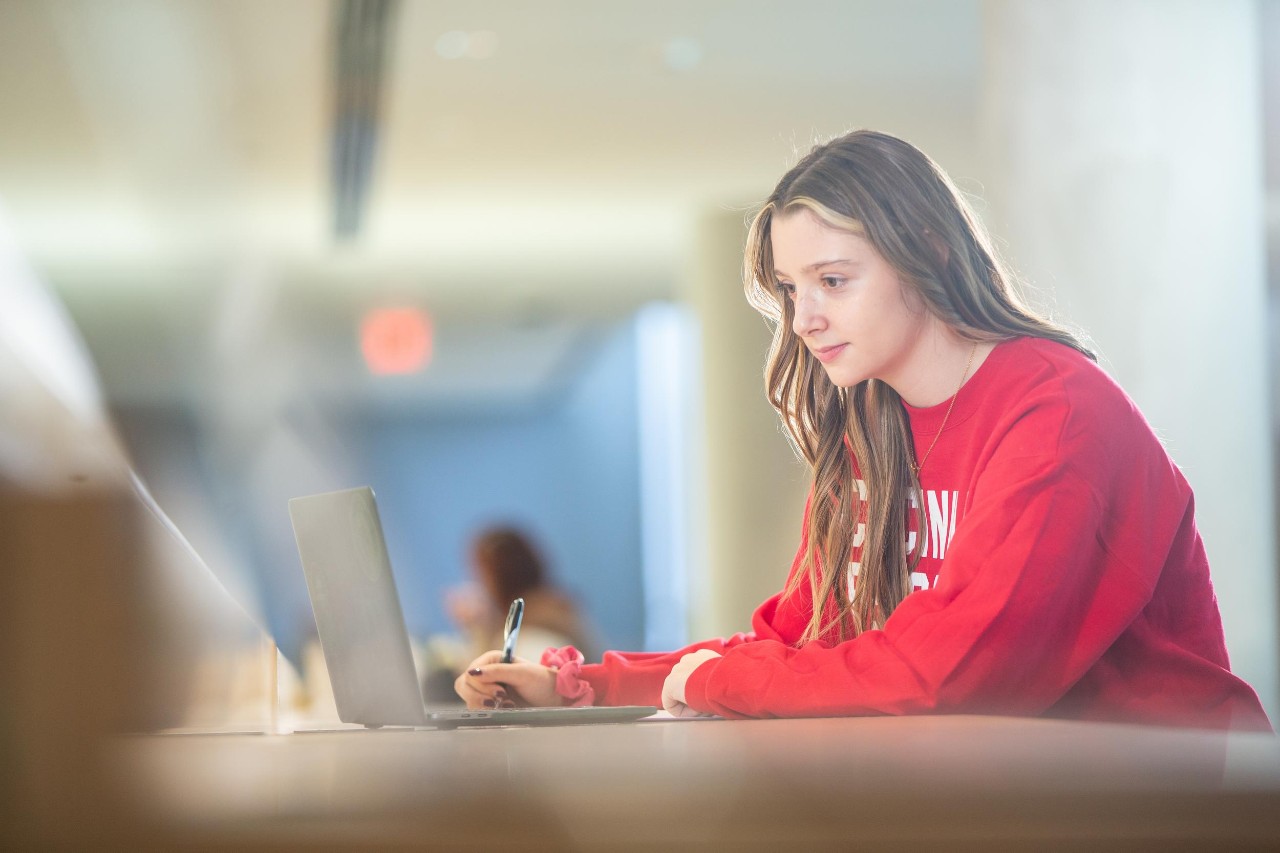 Female student in red sweatshirt using laptop