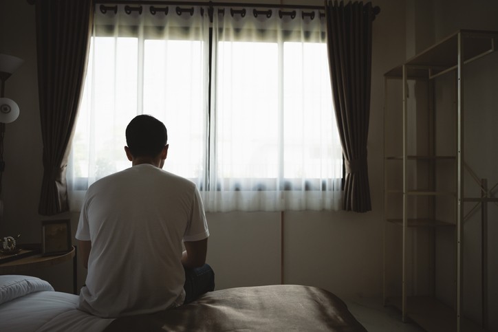 A man sits on a bed and looks out a window