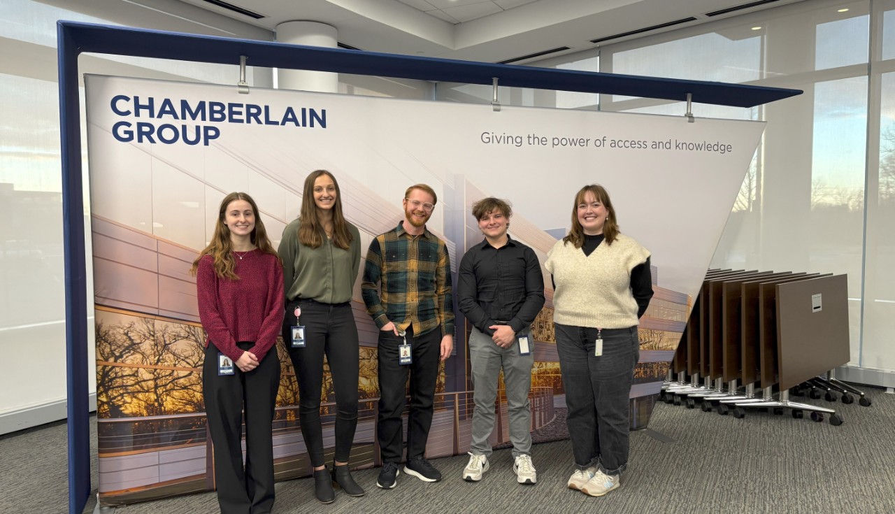 UC graduates and UC co-op students standing in front of a Chamberlain banner