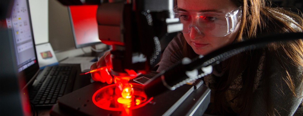 A UC student studies photoexplosive crystals under red light under a microscope.